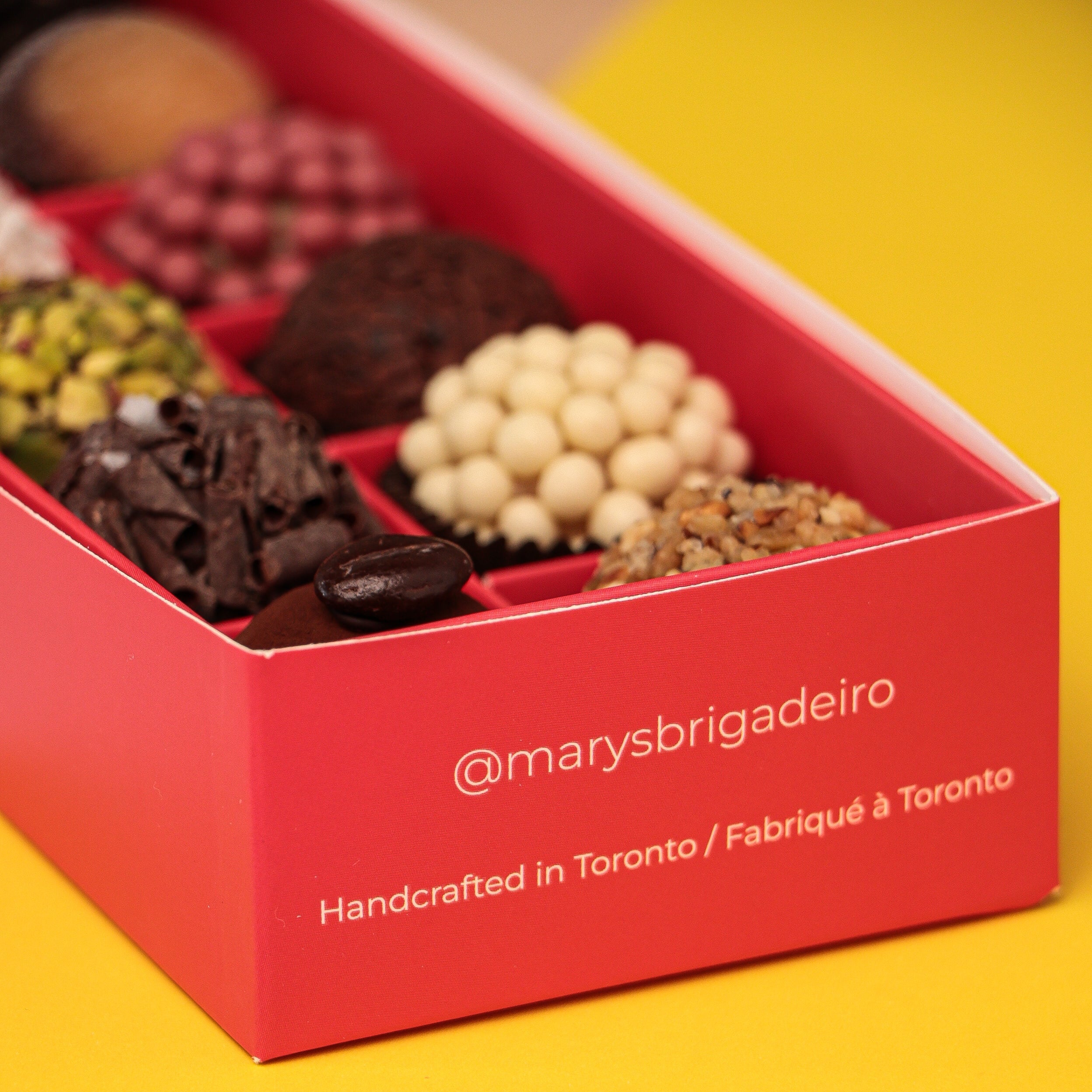 Red box with assorted chocolates on a pink and yellow background, featuring 'marysbrigadeiro' branding.