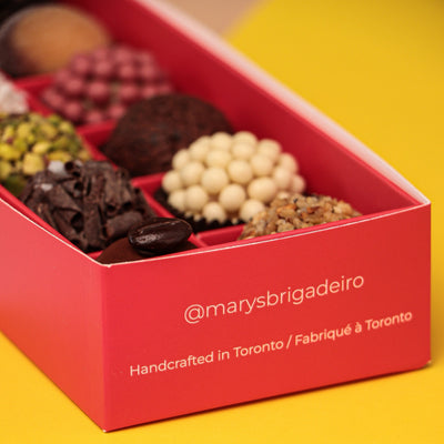 Red box with assorted chocolates on a pink and yellow background, featuring 'marysbrigadeiro' branding.